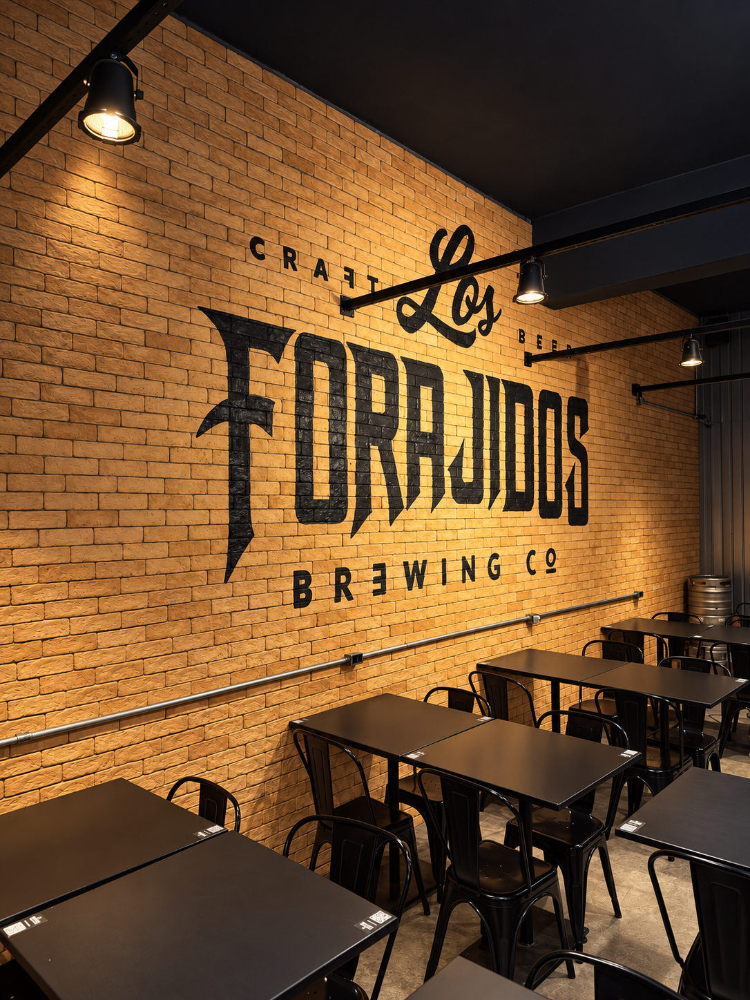 Parede com logo Los Forajidos Brewing Co. e mesas do taproom