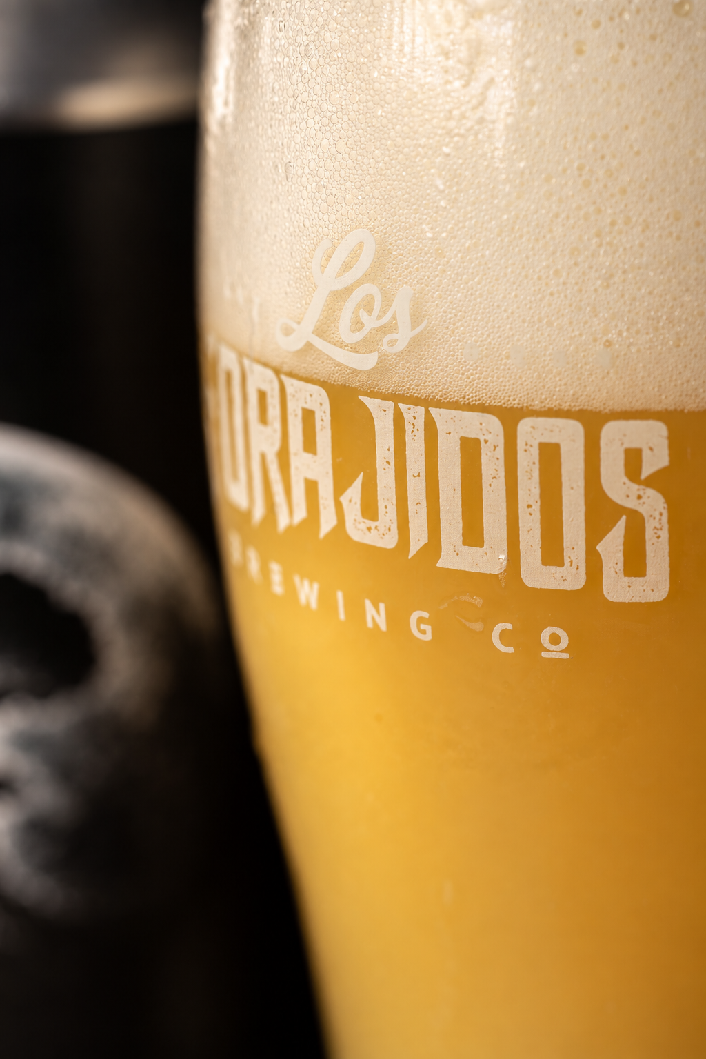 Detalhe do copo Los Forajidos com cerveja dourada e espuma